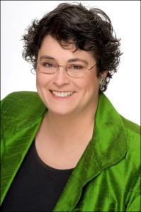 Author photo of mystery author Donna Andrews. A smiling Andrews sports a short haircut and glasses. She's wearing an emerald green blouse over a black shell.